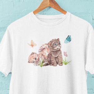 May include: White t-shirt with a watercolor illustration of two kittens playing with butterflies. The kittens are brown and white, and the butterflies are blue, pink, and yellow.