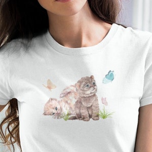 May include: White t-shirt with a watercolor illustration of two kittens and butterflies. The kittens are brown and white and are looking up at the butterflies.