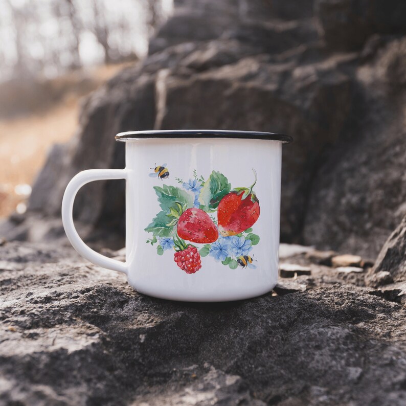 May include: White enamel mug with a black rim and handle. The mug features a watercolour design of strawberries, leaves, and bees.