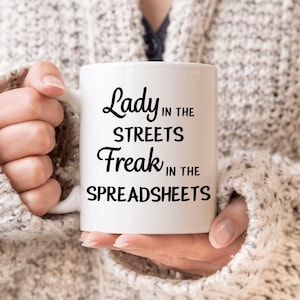 Op de afbeelding: Een witte keramische mok met zwarte tekst die "Lady in the Streets Freak in the Spreadsheets" zegt.