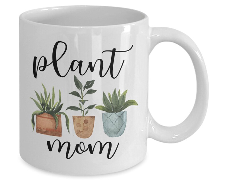 以下が含まれることがあります： 白いセラミック製のコーヒーカップ。黒と白のグラフィックで「plant mom」と書いてあり、緑の葉を持つ鉢植えの植物が3つ描かれています。