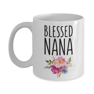May include: White ceramic coffee mug with a black inscription that reads "Blessed Nana" and a floral design in pink, purple, and green.