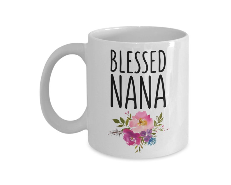 May include: White ceramic coffee mug with a black inscription that reads "Blessed Nana" and a floral design in pink, purple, and green.