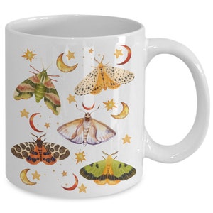 May include: White ceramic mug with a colorful design of moths and stars. The moths are in various shades of green, yellow, orange, and brown. The stars are gold and the background is white.