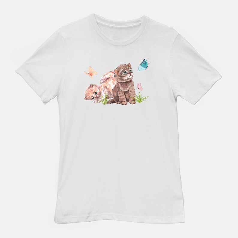 May include: White t-shirt with a watercolor illustration of two brown and orange kittens playing in a field of flowers and butterflies.