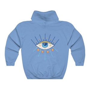 May include: A light blue hooded sweatshirt with a colorful evil eye design on the front. The eye is blue with a white pupil and surrounded by yellow stars and orange and blue rays.