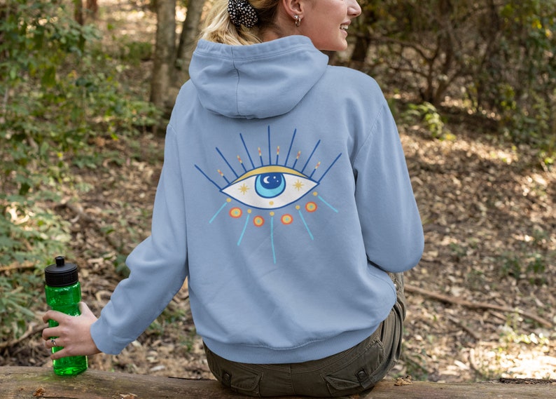 May include: A light blue hooded sweatshirt with a colorful eye design on the back. The eye has blue, yellow, and orange accents.