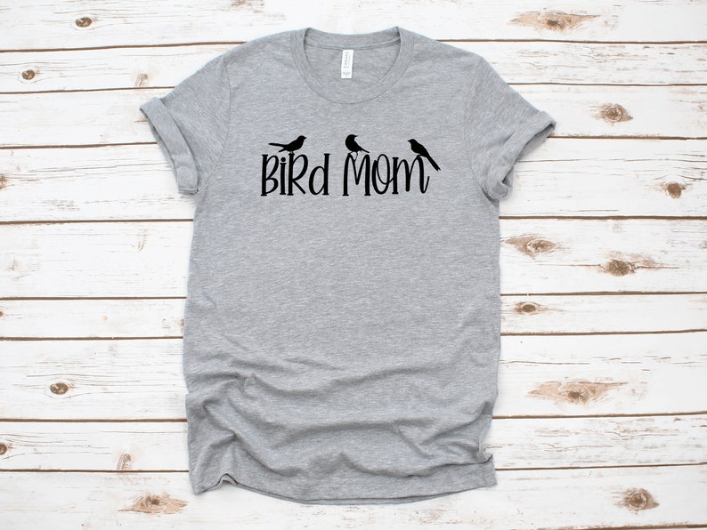 Puede incluir: Una camiseta gris con un gr&aacute;fico negro de tres p&aacute;jaros y el texto "Bird Mom".