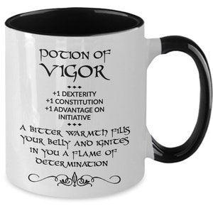 May include: White ceramic mug with a black interior and handle. The mug features the text "POTION OF VIGOR" in a stylized font, along with additional text describing its effects. A decorative flourish is at the bottom of the mug.