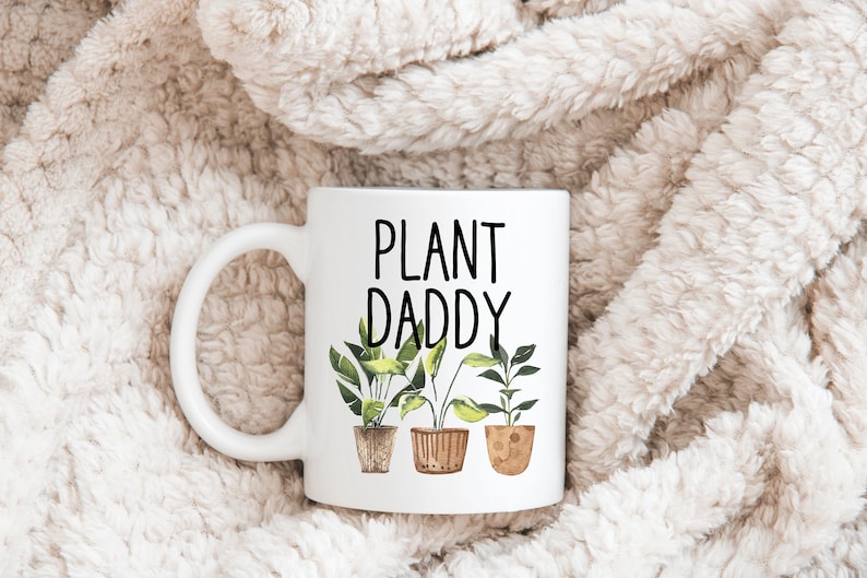 May include: White ceramic mug with a black inscription that reads "PLANT DADDY" and three illustrations of potted plants with green leaves.