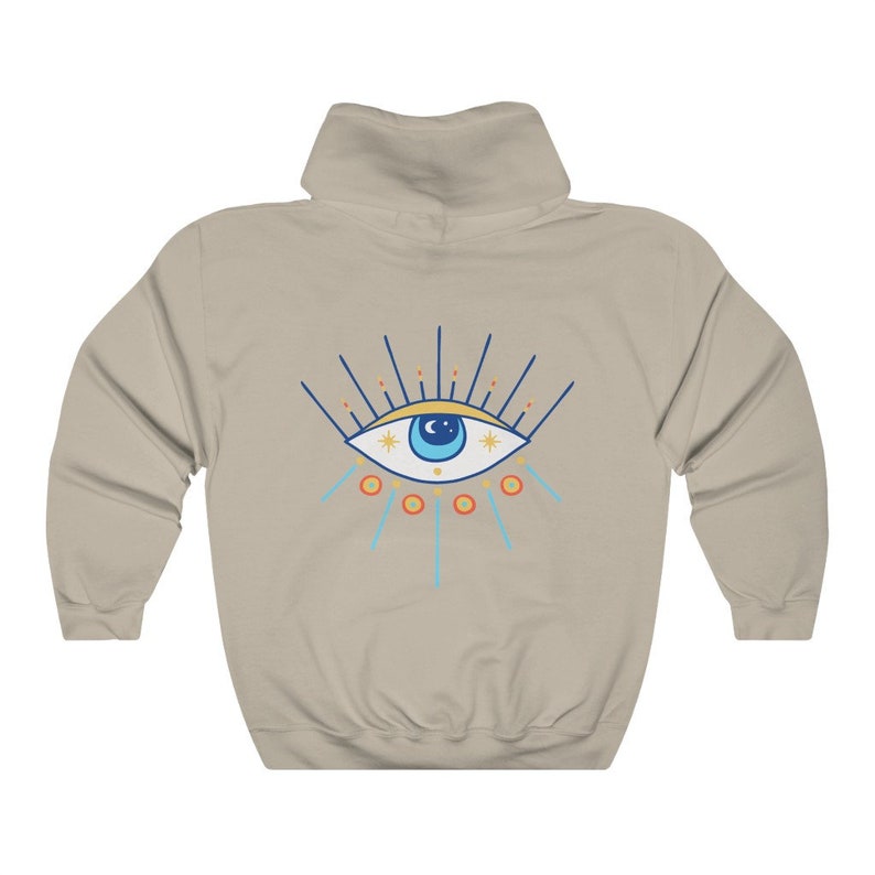 May include: A beige hooded sweatshirt with a blue and yellow evil eye design on the back. The eye has a blue pupil and is surrounded by yellow stars and orange circles.