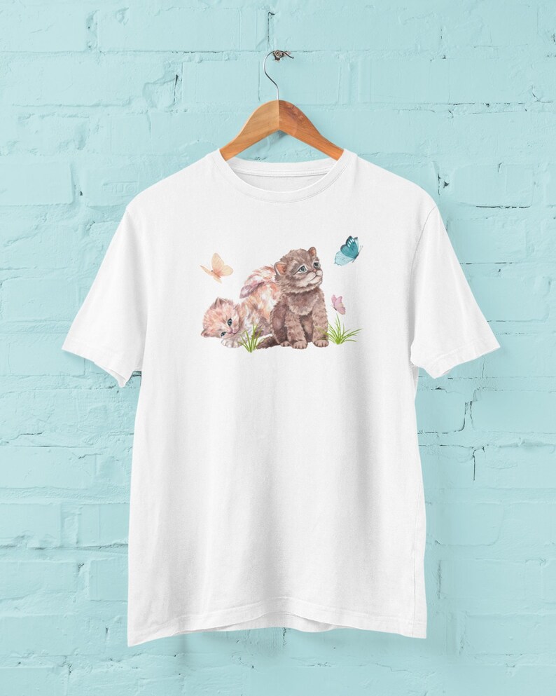 May include: White t-shirt with a watercolor illustration of two kittens playing with butterflies. The kittens are brown and white, and the butterflies are blue, pink, and yellow.