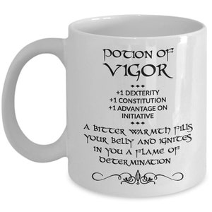 May include: White ceramic mug with a curved handle. The mug features black text that reads "POTION OF VIGOR" and includes game-like attributes. The text also describes the effects of the potion. A decorative flourish is at the bottom.