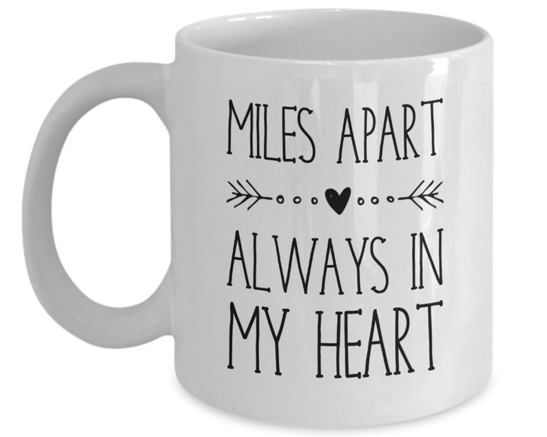Pu&ograve; includere: Tazza da caff&egrave; in ceramica bianca con testo nero che recita "Miles Apart Always In My Heart" con un piccolo cuore e un design a freccia.