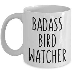 May include: White ceramic coffee mug with black text that reads "BADASS BIRD WATCHER".