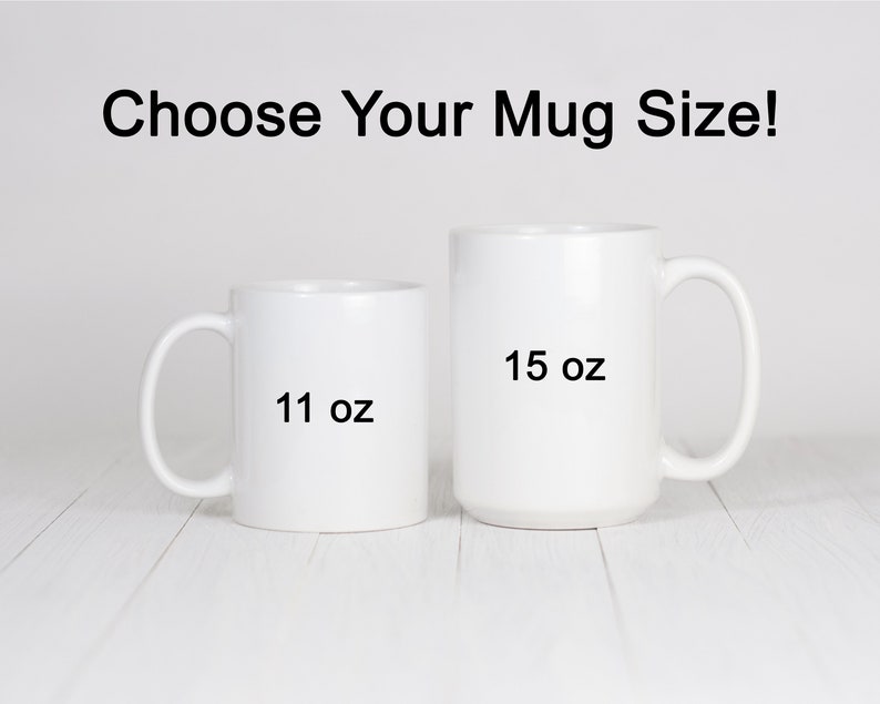 Op de afbeelding: Twee witte keramische mokken, een van 11 oz en een van 15 oz, op een wit houten oppervlak. Kies je mokmaat!