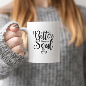 Op de afbeelding: Witte keramische koffiemok met zwarte tekst die "Bitter like my Soul" luidt en een klein zwart koffiekopje-icoon met stoom die eruit komt.