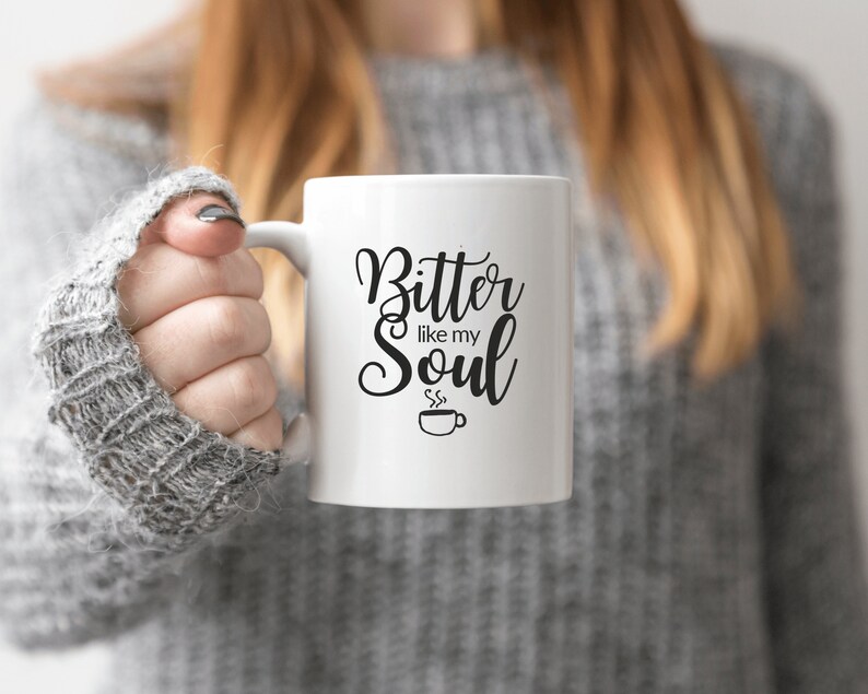 Op de afbeelding: Witte keramische koffiemok met zwarte tekst die "Bitter like my Soul" luidt en een klein zwart koffiekopje-icoon met stoom die eruit komt.