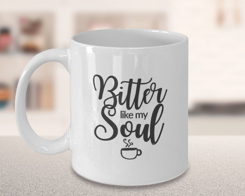 Op de afbeelding: Witte keramische koffiemok met zwarte tekst die "Bitter like my Soul" luidt en een klein zwart koffiekopje-icoon met stoom die eruit komt.