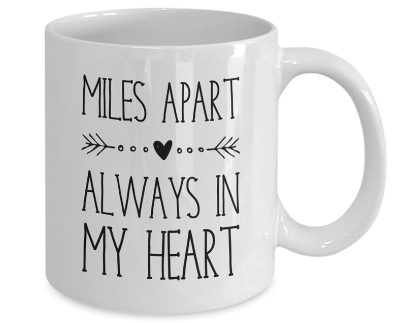 Pu&ograve; includere: Tazza da caff&egrave; in ceramica bianca con testo nero che recita "Miles Apart Always In My Heart" con un piccolo cuore e frecce su entrambi i lati del cuore.