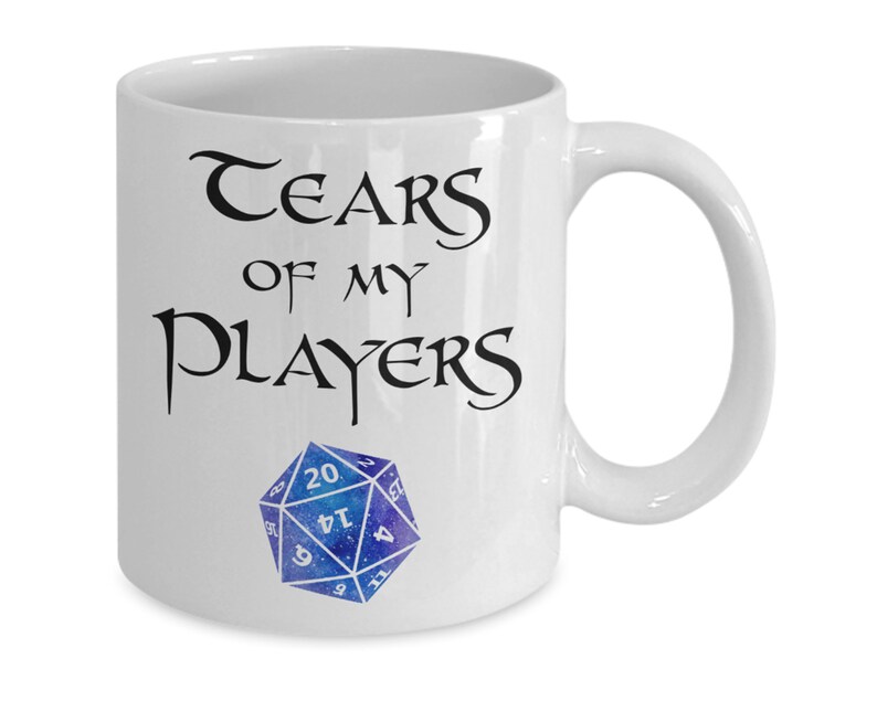 Op de afbeelding: Witte keramische koffiemok met de tekst "Tears of my Players" en een blauwe en paarse 20-zijdige dobbelsteen.