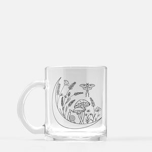 May include: A clear glass mug with a black line drawing of a crescent moon, mushrooms, a snail, flowers, and a moth. The design is on the side of the mug.