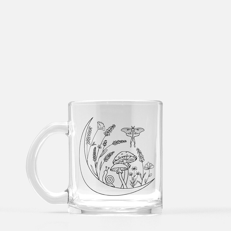 May include: A clear glass mug with a black line drawing of a crescent moon, mushrooms, a snail, flowers, and a moth. The design is on the side of the mug.
