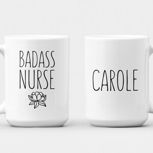 May include: Two white ceramic mugs with black text. One mug says "Badass Nurse" with a small flower design. The other mug says "Carole".