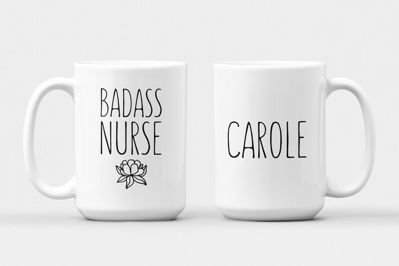 May include: Two white ceramic mugs with black text. One mug says "Badass Nurse" with a small flower design. The other mug says "Carole".