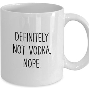 May include: White ceramic coffee mug with black text that reads "Definitely not vodka. Nope."