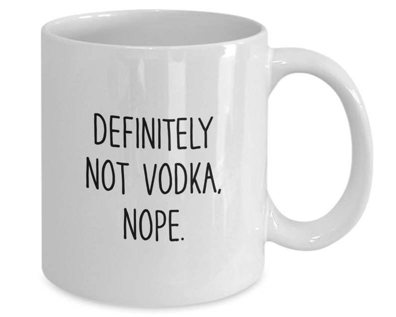 May include: White ceramic coffee mug with black text that reads "Definitely not vodka. Nope."
