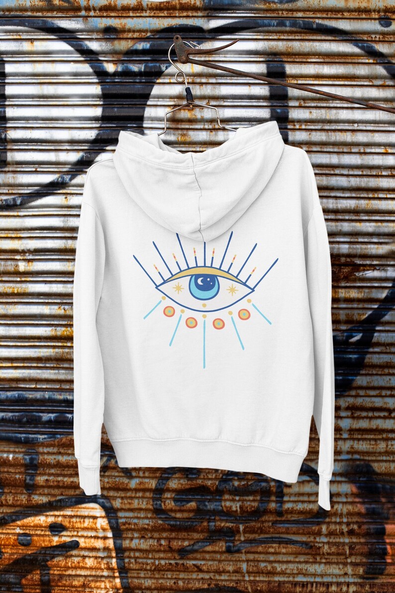 May include: White hooded sweatshirt with a blue eye graphic on the back. The eye has a yellow crescent moon and stars inside. The eye is surrounded by orange and blue rays.