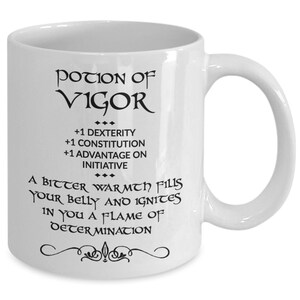 May include: White ceramic mug with the words "POTION OF VIGOR" in black script. The mug also features text that reads "+1 DEXTERITY, +1 CONSTITUTION, +1 ADVANTAGE ON INITIATIVE" and "A BITTER WARMTH FILLS YOUR BELLY AND IGNITES IN YOU A FLAME OF DETERMINATION."