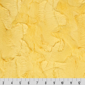 May include: Close-up of a textured, yellow fabric with a soft, plush appearance. The fabric has a wavy, rippled pattern, and a ruler is visible along the bottom edge, with markings from 1 to 15 inches.