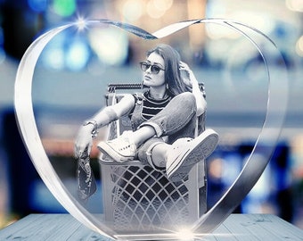 Puede incluir: Un pisapapeles de cristal en forma de corazón con una imagen 3D de una persona con gafas de sol sentada en un carrito de la compra.