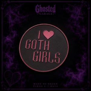 Op de afbeelding: Een ronde zwarte patch met een donkerroze rand met de tekst I GOTH GIRLS in een gestileerd lettertype en een roze hartpictogram. Het ontwerp is gecentreerd op een donkere achtergrond met paarse rookeffecten en de tekst GHOSTED GARAGE bovenaan.