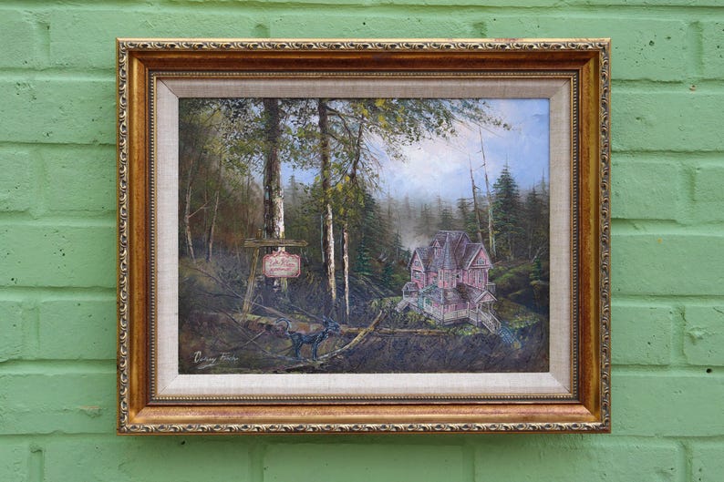 May include: An oil painting in a gold ornate frame depicts a forest scene with a pink house and a sign. The painting features a house with a porch, trees, and a sign with text. The artwork is framed in a gold-colored frame.