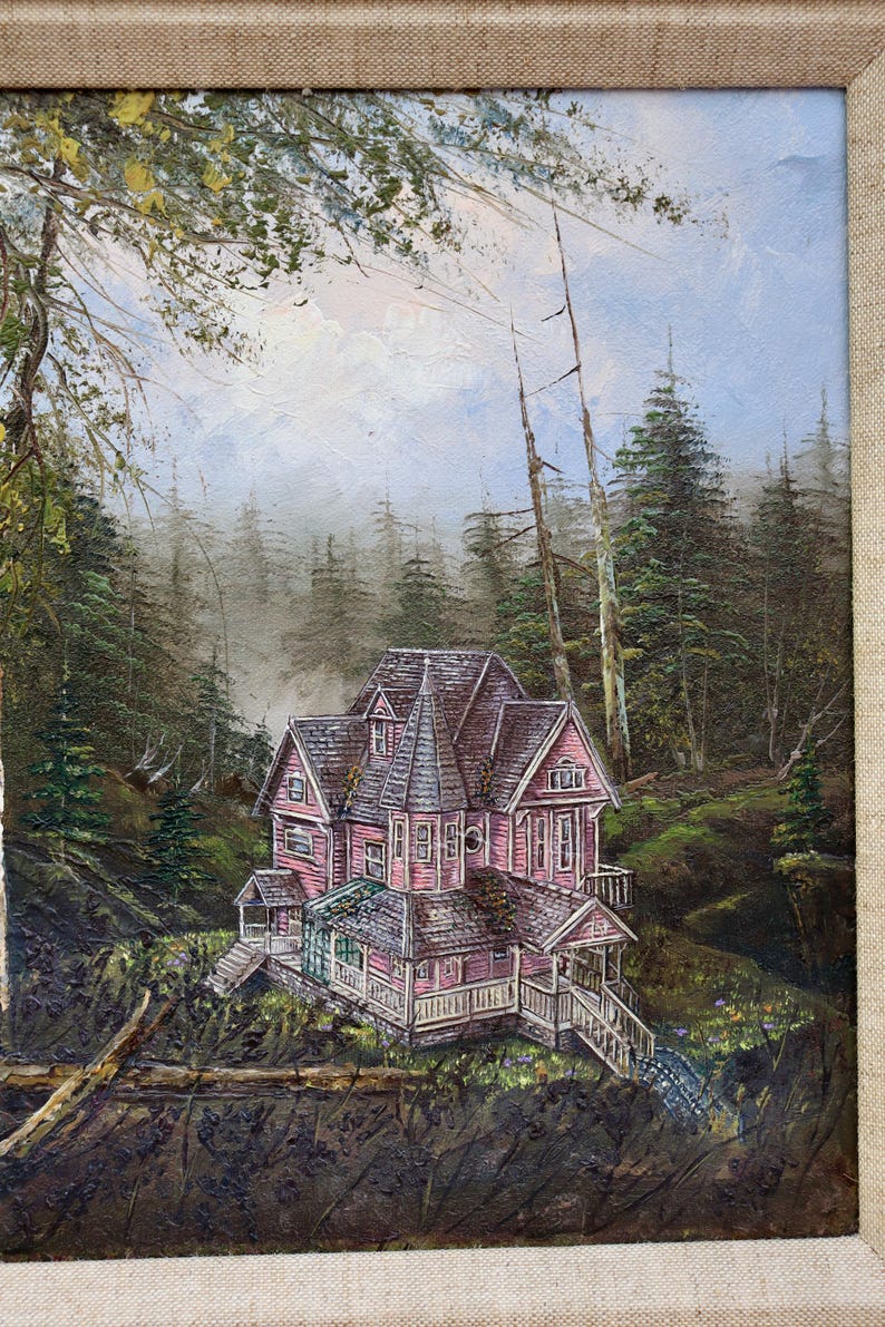 May include: Oil painting of a pink Victorian house nestled in a forest. The house has multiple gables and a wraparound porch. The artwork is framed with a neutral linen-textured border, and the background features tall evergreen trees.