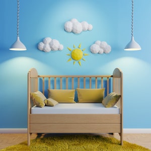 Puede incluir: Una cuna de madera con un colchón blanco y almohadas amarillas. La cuna está decorada con nubes de papel y un recorte de sol en una pared azul claro.