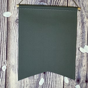 Puede incluir: Una pancarta de tela verde oscuro colgada de una pared de madera. La pancarta tiene un borde festoneado y está en blanco.