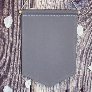 May include: A gray fabric banner with a scalloped edge hangs from a wooden dowel against a rustic wood background. The banner is blank and ready for customization.