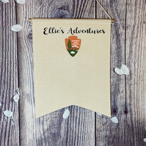May include: A beige canvas banner with the text "Ellie's Adventures" and a National Park Service logo. The banner is hanging on a wooden wall.