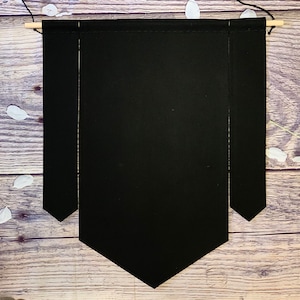 Op de afbeelding: Een zwarte stoffen banner met een puntige onderkant, hangend aan een houten stok.
