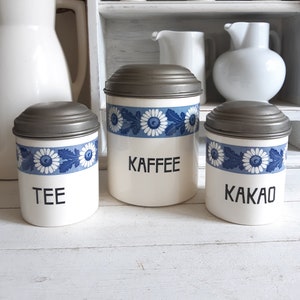 May include: Three vintage ceramic canisters with blue and white floral designs and silver lids. The canisters are labeled "Tee", "Kaffee", and "Kakao".