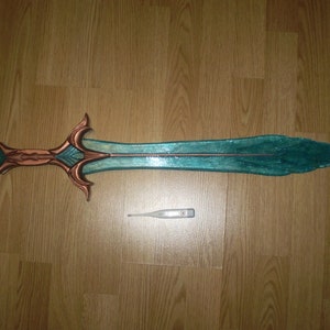 May include: A teal and copper colored sword with a decorative handle. The sword is about 30 inches long and is lying on a wooden floor.