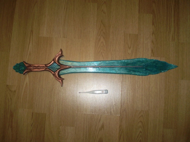May include: A teal and copper colored sword with a decorative handle. The sword is about 30 inches long and is lying on a wooden floor.