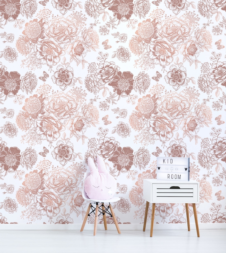 May include: A white wall with a rose gold floral pattern wallpaper. A white bedside table with a light box that says "KID ROOM" is on the right side of the image. A white chair with a pink bunny rabbit cushion is on the left side of the image.
