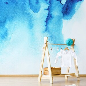 Puede incluir: Un perchero de madera con una camisa blanca colgada. El perchero tiene una peque&ntilde;a caja de madera en el estante inferior y una cadena de luces colgando de la parte superior. El fondo es una pared azul de acuarela.
