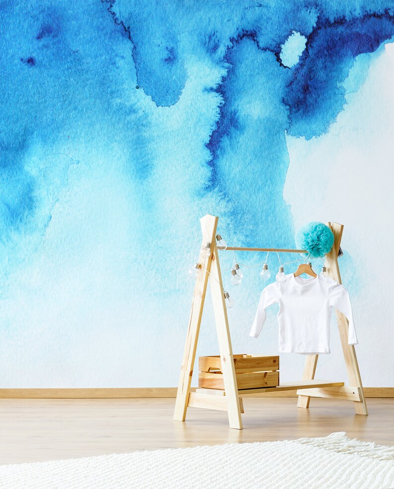 Puede incluir: Un perchero de madera con una camisa blanca colgada. El perchero tiene una peque&ntilde;a caja de madera en el estante inferior y una cadena de luces colgando de la parte superior. El fondo es una pared azul de acuarela.