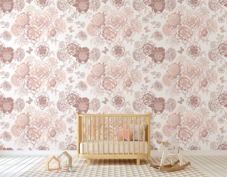May include: A nursery room with a white wall covered in a floral wallpaper pattern in shades of pink and brown. A wooden cot with a pink pillow is in the foreground. A rocking horse is on the floor.